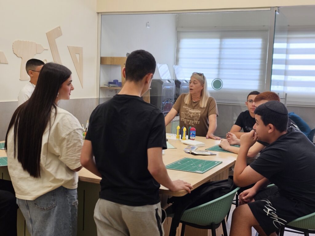 מורה יושבת עם קבוצת תלמידים סביב שולחן עבודה