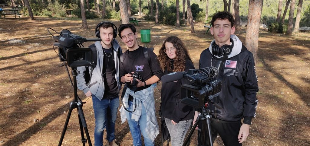 ארבעה תלמידי מגמת מדיה מחייכים עם מצלמות בצילומי שטח